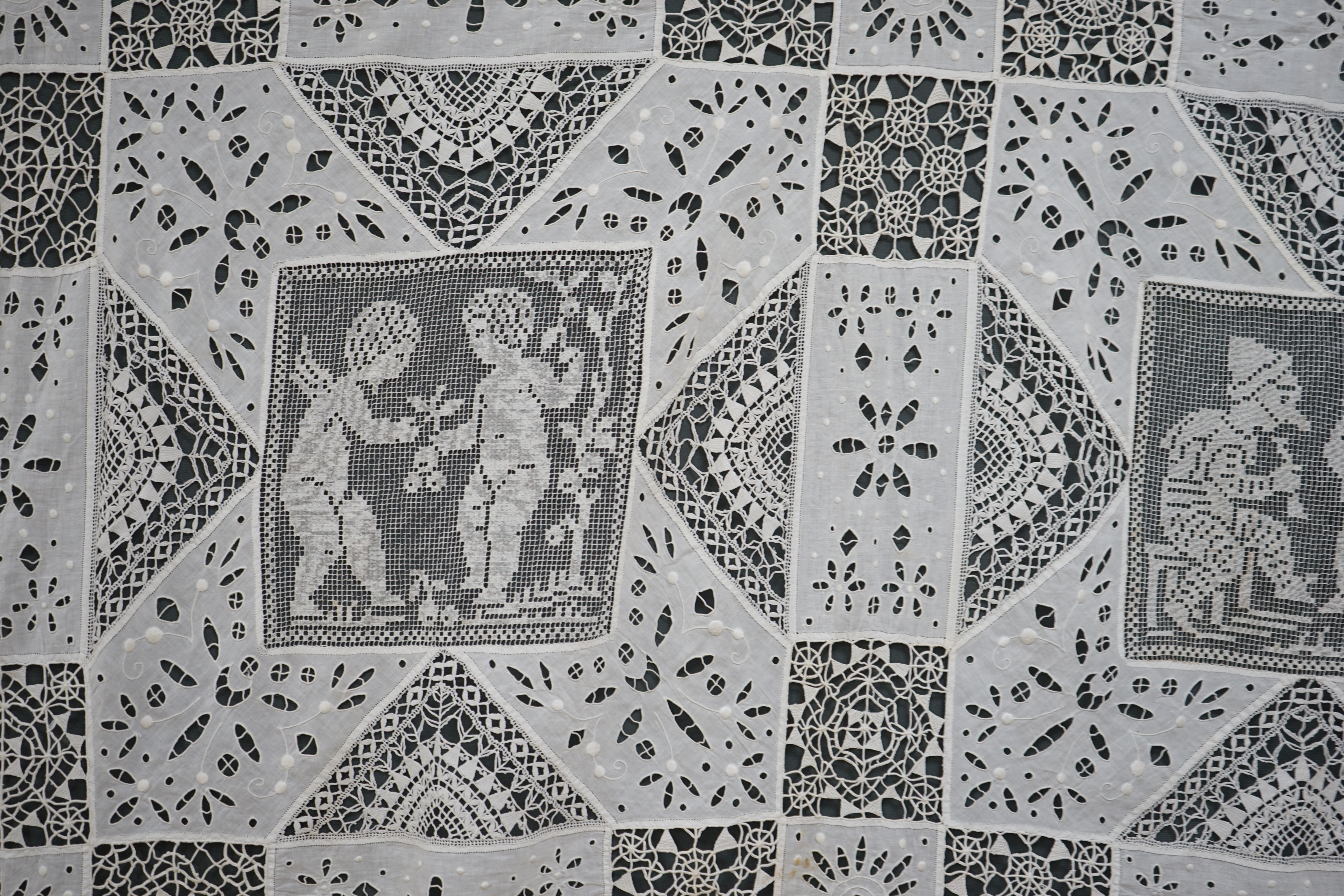An early 20th century Italian bedcover, worked with fillet lace insertions of putti, white multi patterned fine linen cut work squares and similar multi patterned hand needle lace insertions, creating a unique and totall